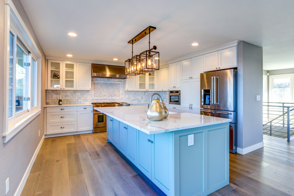 This is an example of a mid-sized transitional u-shaped eat-in kitchen in Los Angeles with a farmhouse sink, shaker cabinets, white cabinets, quartz benchtops, white splashback, marble splashback, stainless steel appliances, medium hardwood floors, with island, beige floor and white benchtop.
