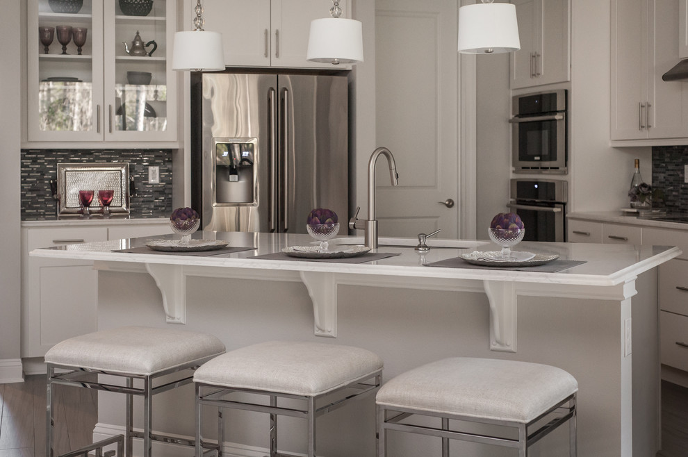 Example of a large transitional l-shaped ceramic tile eat-in kitchen design in Jacksonville with a drop-in sink, flat-panel cabinets, white cabinets, granite countertops, black backsplash, glass tile backsplash, stainless steel appliances and an island