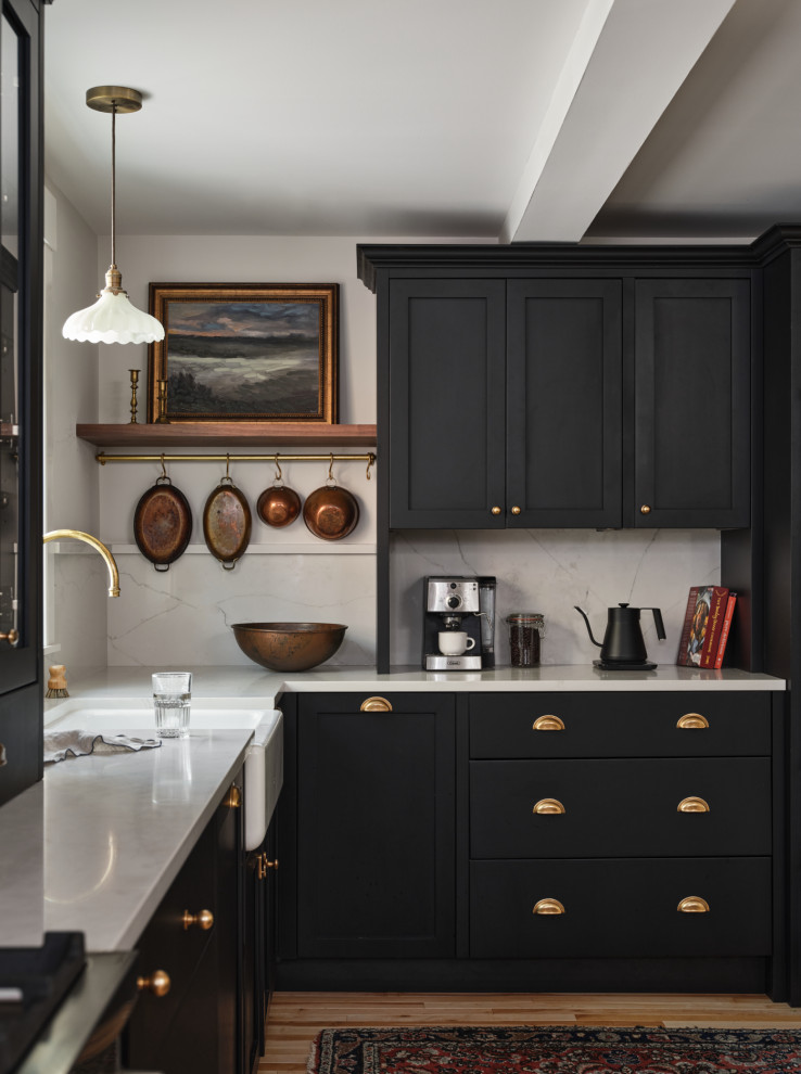 Design ideas for a mid-sized traditional l-shaped kitchen in Portland Maine with a farmhouse sink, black cabinets, quartz benchtops, white splashback, engineered quartz splashback, black appliances, light hardwood floors, white benchtop, shaker cabinets and beige floor.