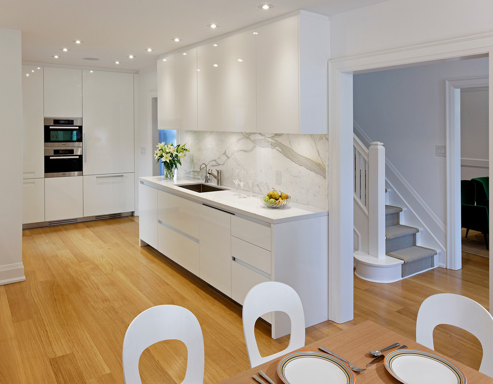 Mid-sized contemporary galley eat-in kitchen in Toronto with an undermount sink, flat-panel cabinets, white cabinets, quartz benchtops, stone slab splashback, panelled appliances, medium hardwood floors and no island.