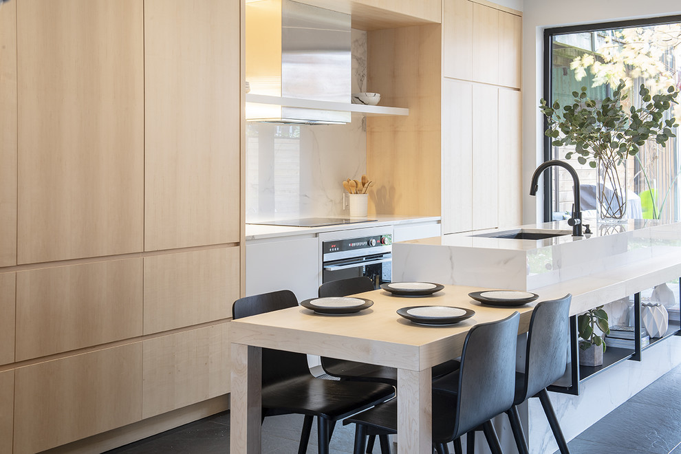 Mid-sized contemporary single-wall eat-in kitchen in Montreal with an undermount sink, flat-panel cabinets, light wood cabinets, solid surface benchtops, white splashback, marble splashback, panelled appliances, porcelain floors, with island, black floor and white benchtop.