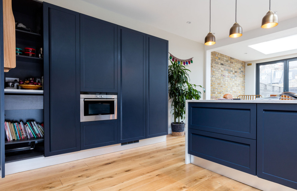 Inspiration for a mid-sized traditional l-shaped eat-in kitchen in London with an undermount sink, shaker cabinets, blue cabinets, quartzite benchtops, white splashback, engineered quartz splashback, panelled appliances, light hardwood floors, a peninsula, brown floor and yellow benchtop.