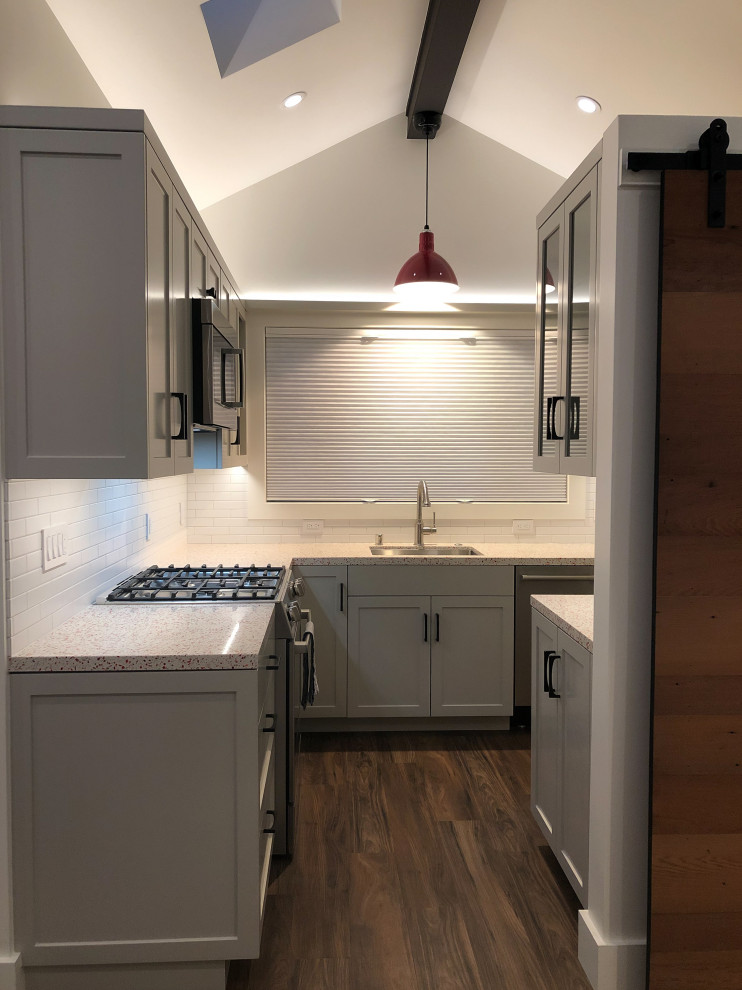 Inspiration for a small arts and crafts u-shaped kitchen in San Francisco with an undermount sink, shaker cabinets, brown cabinets, quartz benchtops, white splashback, ceramic splashback, stainless steel appliances, laminate floors, no island, brown floor, red benchtop and exposed beam.