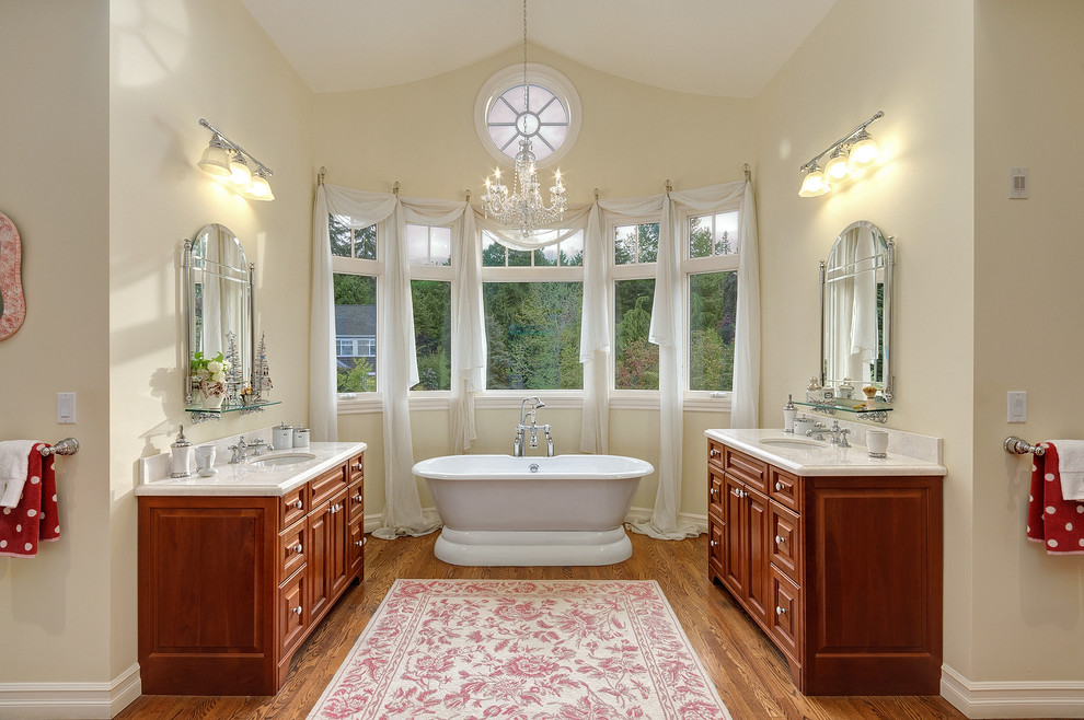 Inspiration for a large beach style master bathroom in Seattle with a freestanding tub, raised-panel cabinets, medium wood cabinets, quartzite benchtops, yellow walls and medium hardwood floors.