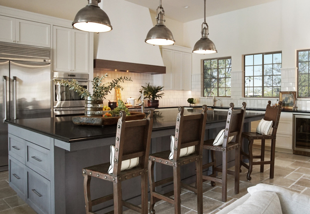 This is an example of a large transitional l-shaped eat-in kitchen in Phoenix with an integrated sink, recessed-panel cabinets, white cabinets, granite benchtops, white splashback, ceramic splashback, stainless steel appliances, limestone floors, with island, beige floor, black benchtop and coffered.
