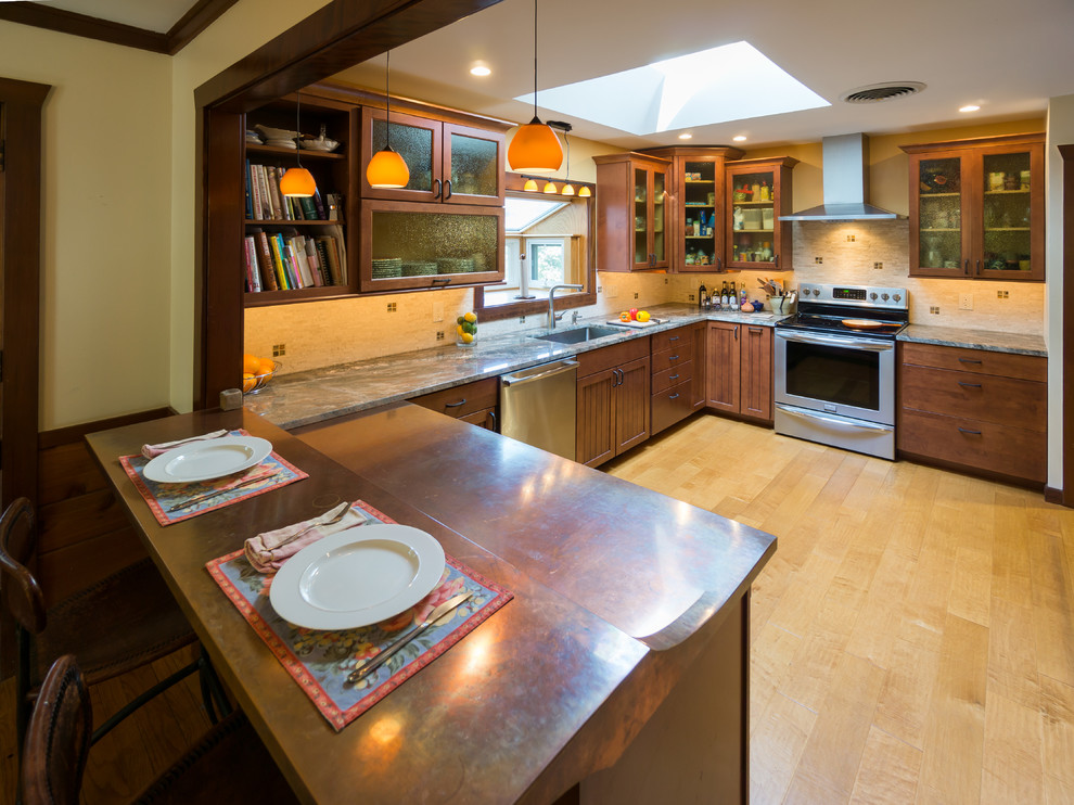 This is an example of a transitional u-shaped eat-in kitchen in Providence with an undermount sink, glass-front cabinets, medium wood cabinets, granite benchtops, beige splashback, stone tile splashback and stainless steel appliances.