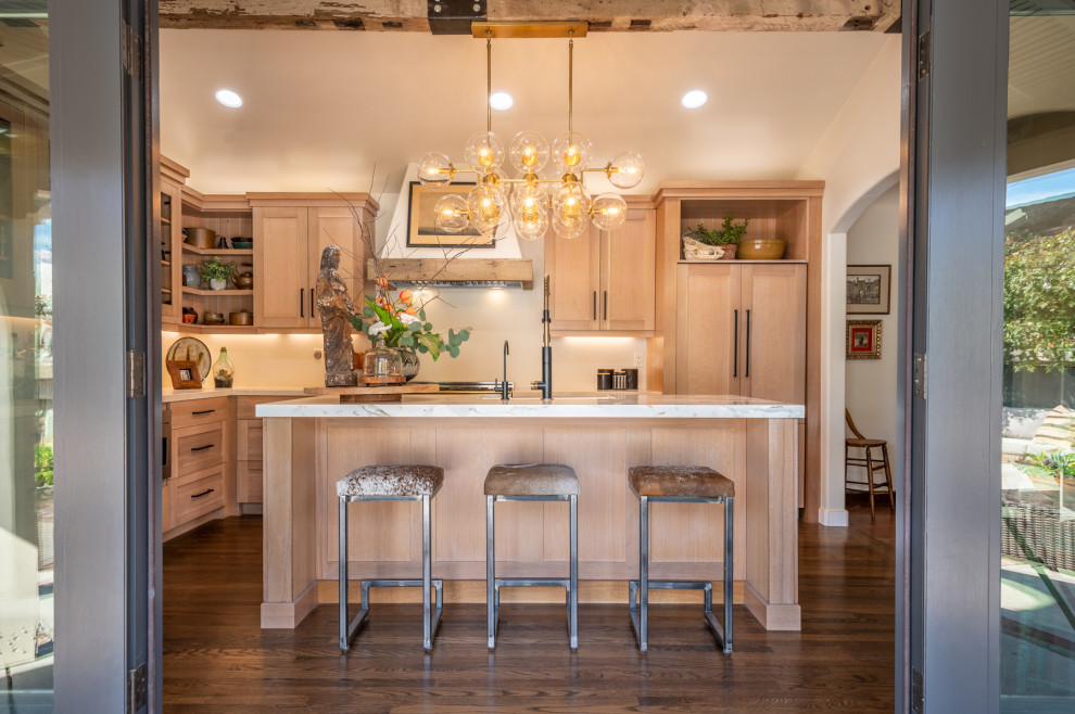 This is an example of a mid-sized arts and crafts l-shaped eat-in kitchen in Sacramento with a farmhouse sink, shaker cabinets, light wood cabinets, limestone benchtops, beige splashback, porcelain splashback, stainless steel appliances, medium hardwood floors, with island, brown floor, beige benchtop and vaulted.
