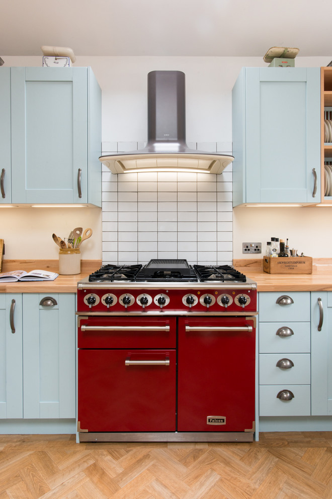 This is an example of a large country u-shaped eat-in kitchen in Other with a double-bowl sink, shaker cabinets, blue cabinets, wood benchtops, white splashback, subway tile splashback, light hardwood floors and no island.