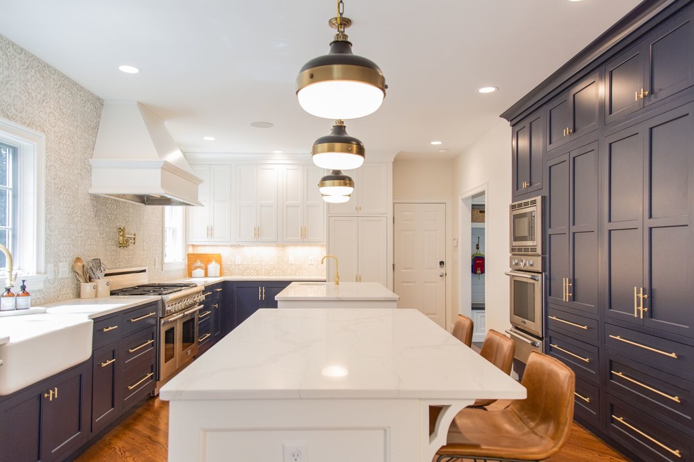 Design ideas for a transitional u-shaped kitchen in Boston with a farmhouse sink, shaker cabinets, blue cabinets, grey splashback, stainless steel appliances, medium hardwood floors, multiple islands and brown floor.