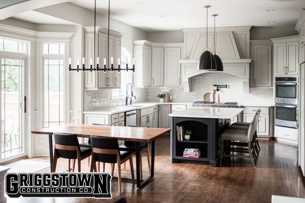 This is an example of a large modern l-shaped eat-in kitchen in Other with a single-bowl sink, raised-panel cabinets, white cabinets, quartz benchtops, white splashback, ceramic splashback, stainless steel appliances, dark hardwood floors, with island, brown floor and white benchtop.