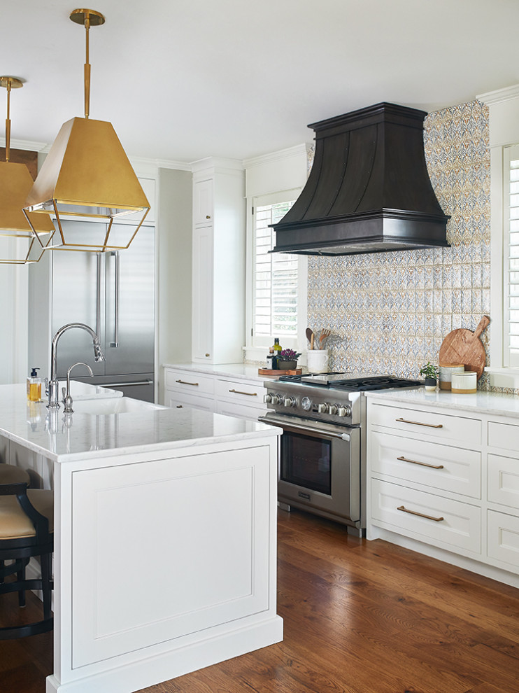 Inspiration for a mid-sized beach style l-shaped open plan kitchen in Grand Rapids with a farmhouse sink, shaker cabinets, white cabinets, quartz benchtops, multi-coloured splashback, terra-cotta splashback, stainless steel appliances, medium hardwood floors, with island, brown floor and white benchtop.