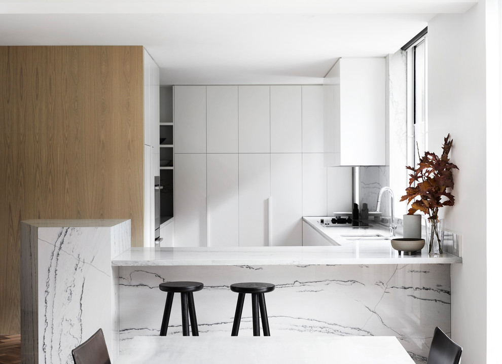 Inspiration for a contemporary u-shaped kitchen in Melbourne with a double-bowl sink, flat-panel cabinets, white cabinets, white splashback, stone slab splashback, a peninsula and white benchtop.
