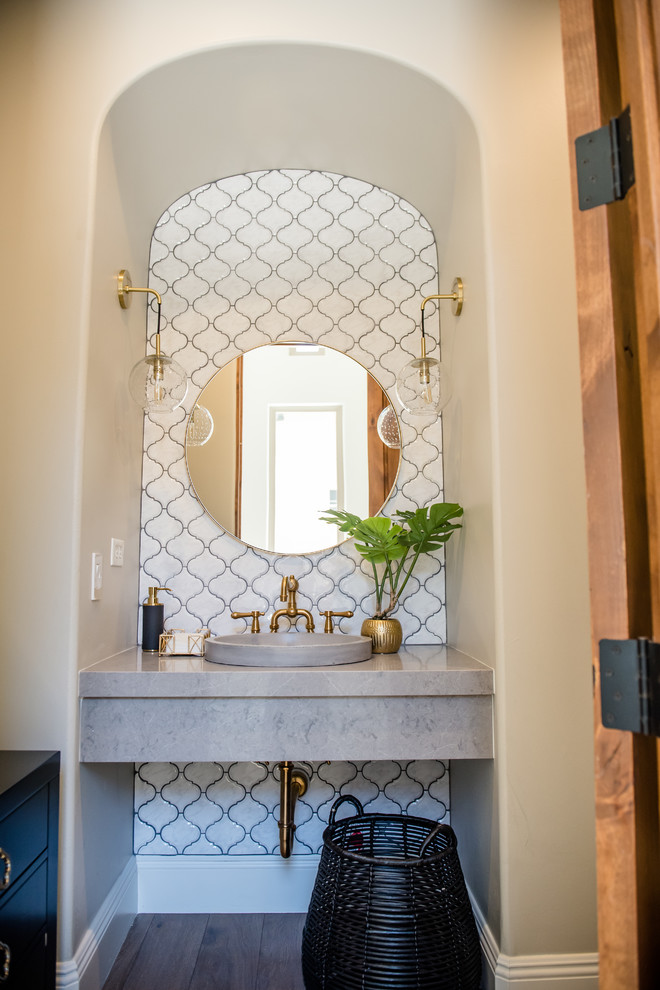 Photo of a mid-sized eclectic powder room in Phoenix with white tile, ceramic tile, grey walls, medium hardwood floors, a vessel sink, engineered quartz benchtops and grey benchtops.