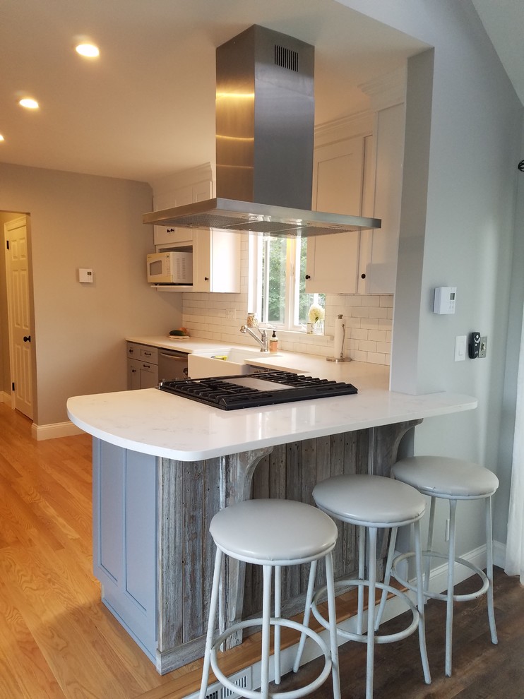 Inspiration for a small transitional light wood floor and beige floor kitchen remodel in Providence with a farmhouse sink, shaker cabinets, white cabinets, marble countertops, white backsplash, subway tile backsplash, stainless steel appliances, a peninsula and white countertops