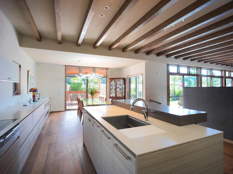 Inspiration for an expansive contemporary galley separate kitchen in Other with a single-bowl sink, flat-panel cabinets, beige cabinets, medium hardwood floors, with island, brown floor, solid surface benchtops, beige splashback, black appliances and beige benchtop.