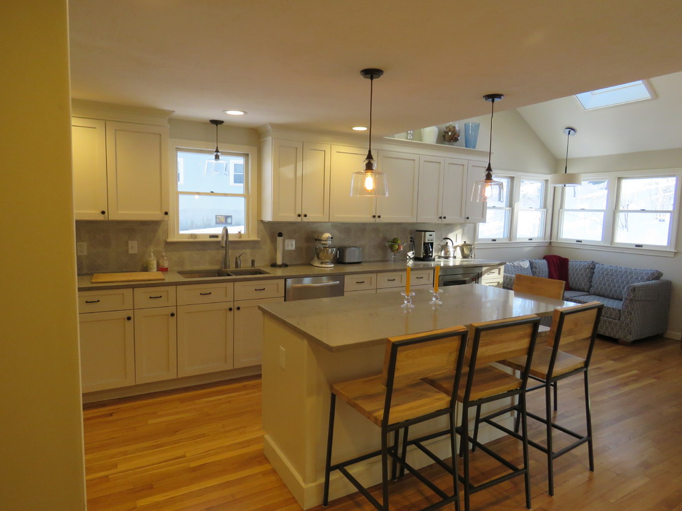 Large transitional l-shaped medium tone wood floor open concept kitchen photo in Boston with an undermount sink, shaker cabinets, white cabinets, quartz countertops, gray backsplash, stainless steel appliances and an island