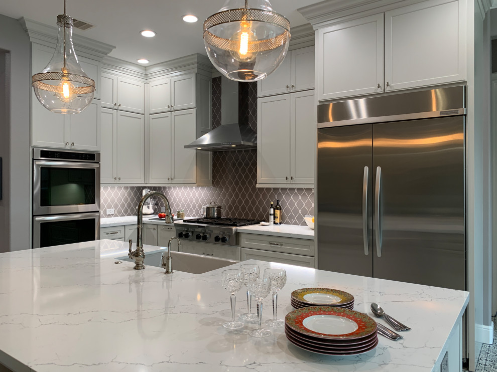 Inspiration for a transitional l-shaped porcelain tile and multicolored floor kitchen remodel in Houston with a farmhouse sink, recessed-panel cabinets, white cabinets, quartz countertops, gray backsplash, ceramic backsplash, stainless steel appliances, an island and white countertops
