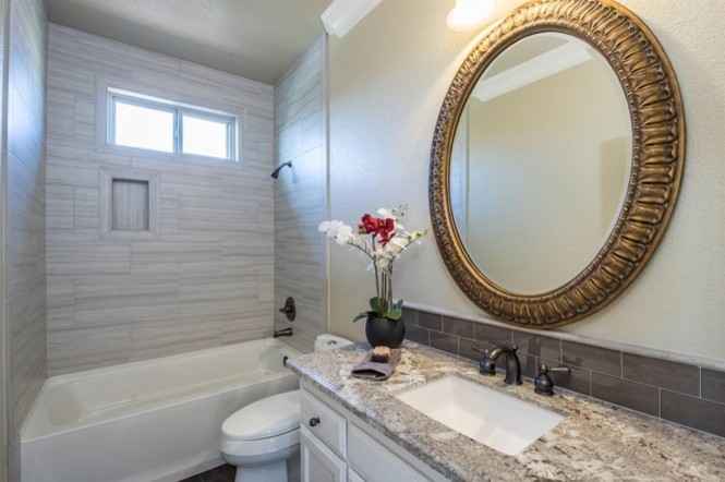 Photo of a mid-sized contemporary 3/4 bathroom in Other with raised-panel cabinets, white cabinets, gray tile, glass sheet wall, an undermount sink, granite benchtops, an alcove tub, a shower/bathtub combo, a two-piece toilet, beige walls, brown floor, a shower curtain and dark hardwood floors.