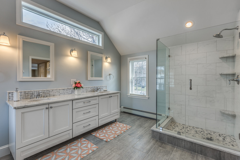 This is an example of a large transitional master bathroom in Boston with beaded inset cabinets, white cabinets, a corner shower, white tile, marble, white walls, porcelain floors, an undermount sink, marble benchtops, grey floor and a hinged shower door.