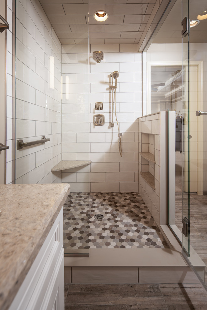 Design ideas for a mid-sized transitional master bathroom in Omaha with recessed-panel cabinets, white cabinets, a corner shower, a two-piece toilet, white tile, ceramic tile, beige walls, porcelain floors, an undermount sink, engineered quartz benchtops, brown floor, a hinged shower door and beige benchtops.