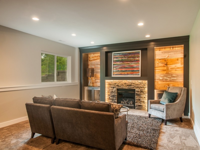This is an example of a mid-sized country look-out basement in Cedar Rapids with beige walls, medium hardwood floors, a standard fireplace, a stone fireplace surround and brown floor.