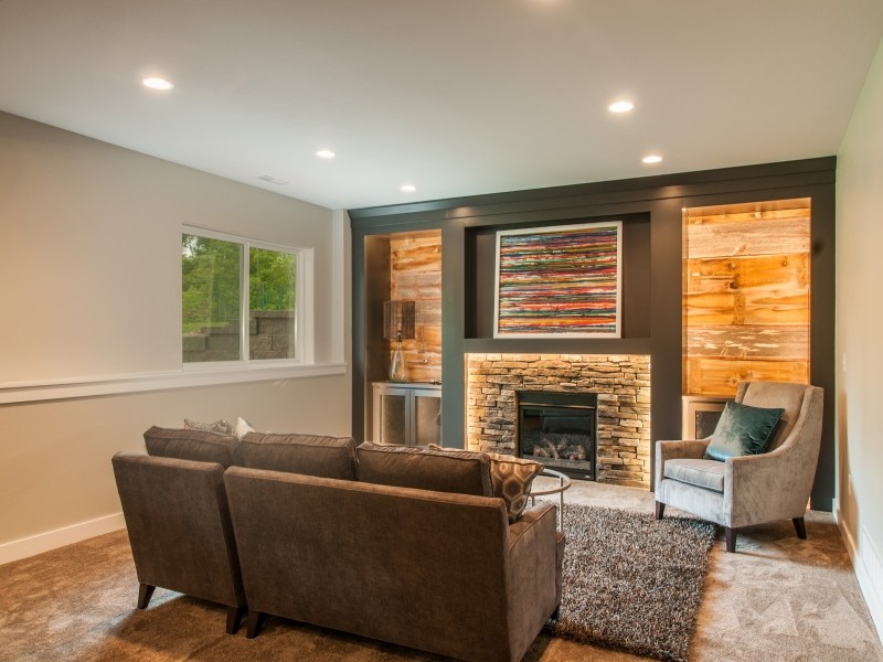 Mid-sized mountain style look-out medium tone wood floor and brown floor basement photo in Cedar Rapids with beige walls, a standard fireplace and a stone fireplace