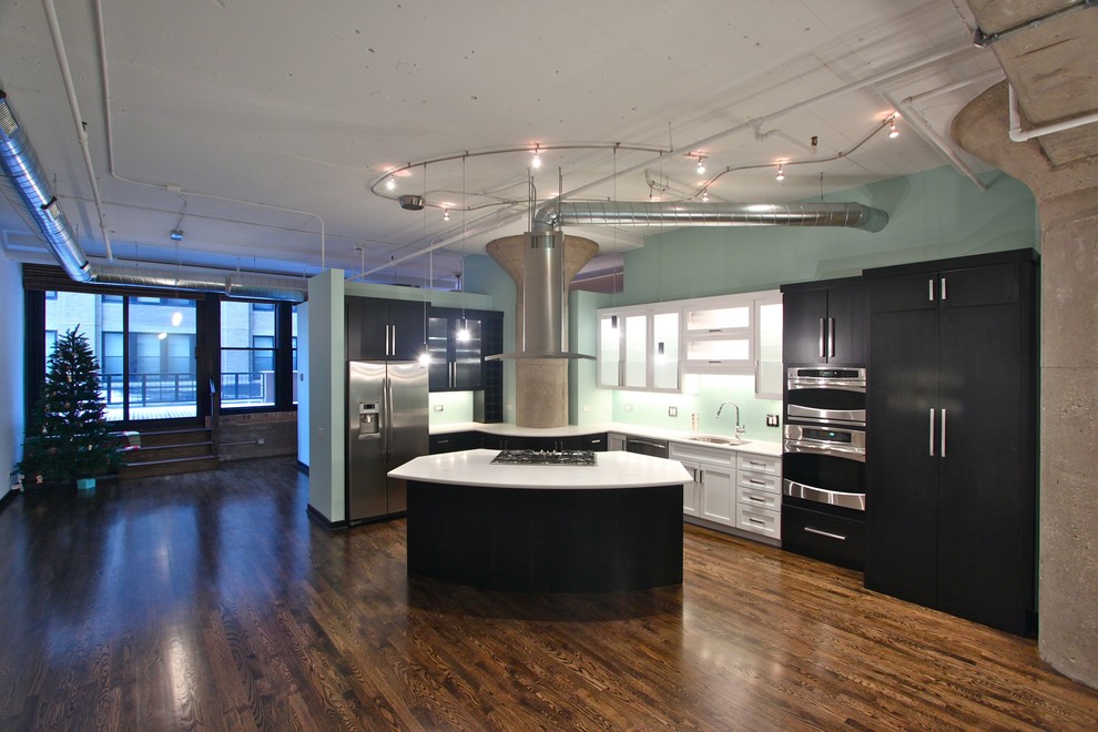 Industrial l-shaped kitchen in Chicago with flat-panel cabinets, black cabinets, blue splashback, glass sheet splashback and stainless steel appliances.