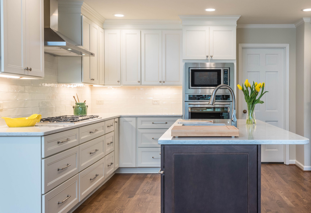 Mid-sized beach style l-shaped separate kitchen in Atlanta with a farmhouse sink, recessed-panel cabinets, white cabinets, marble benchtops, white splashback, subway tile splashback, stainless steel appliances, medium hardwood floors, with island, brown floor and white benchtop.