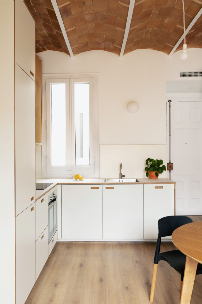 Photo of a mid-sized mediterranean l-shaped separate kitchen in Other with an integrated sink, shaker cabinets, white cabinets, laminate benchtops, white splashback, ceramic splashback, stainless steel appliances, plywood floors, brown floor, white benchtop and coffered.