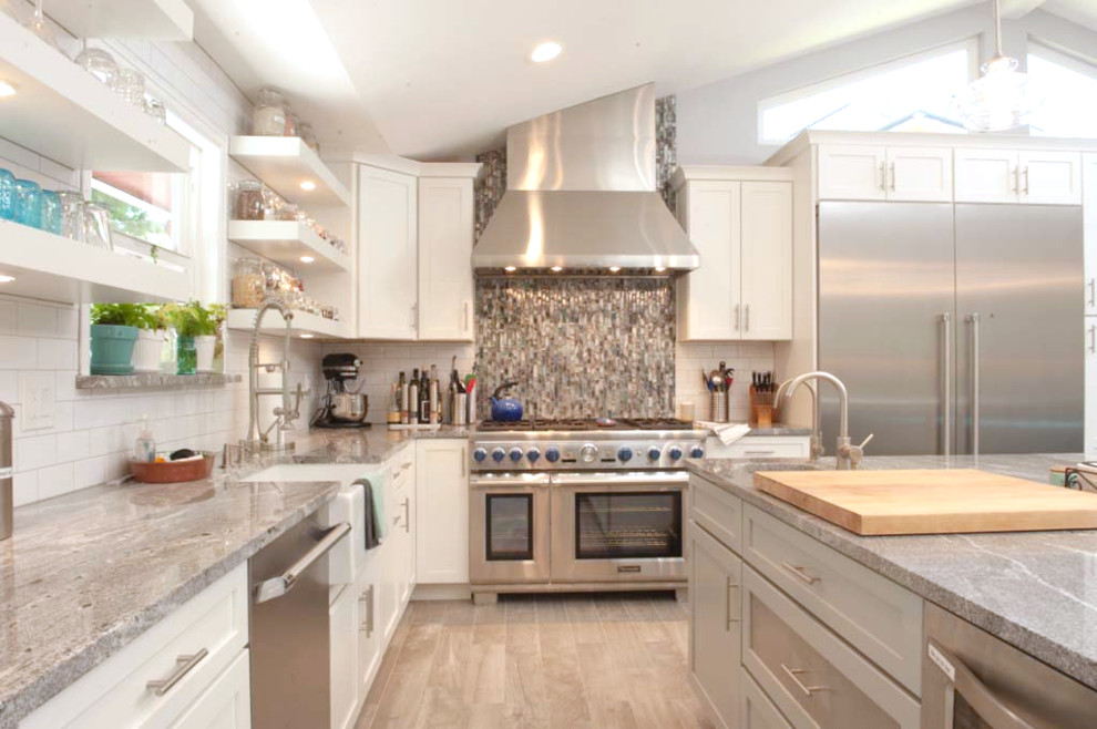 This is an example of a large country l-shaped open plan kitchen in Denver with a farmhouse sink, shaker cabinets, white cabinets, granite benchtops, white splashback, subway tile splashback, stainless steel appliances, light hardwood floors, with island, beige floor and grey benchtop.