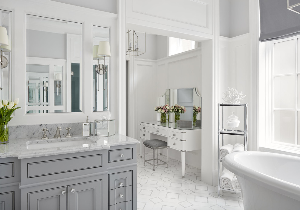 Photo of a large transitional master bathroom in Chicago with recessed-panel cabinets, grey cabinets, a freestanding tub, a two-piece toilet, grey walls, ceramic floors, an undermount sink, marble benchtops, white floor and grey benchtops.