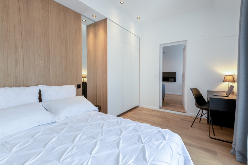 Ejemplo de dormitorio actual de tamaño medio con paredes blancas y suelo de madera clara