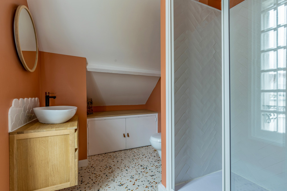 Пример оригинального дизайна: ванная комната среднего размера в современном стиле с плоскими фасадами, белыми фасадами, угловым душем, белой плиткой, керамической плиткой, оранжевыми стенами, полом из терраццо, душевой кабиной, раковиной с несколькими смесителями, столешницей из дерева, разноцветным полом, коричневой столешницей, тумбой под одну раковину и встроенной тумбой