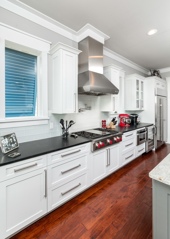 Photo of a mid-sized beach style galley open plan kitchen in Atlanta with an undermount sink, shaker cabinets, white cabinets, wood benchtops, white splashback, porcelain splashback, stainless steel appliances, dark hardwood floors and with island.