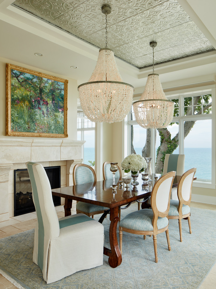 This is an example of a mid-sized beach style separate dining room in Chicago with beige walls, limestone floors, a standard fireplace, a tile fireplace surround and beige floor.