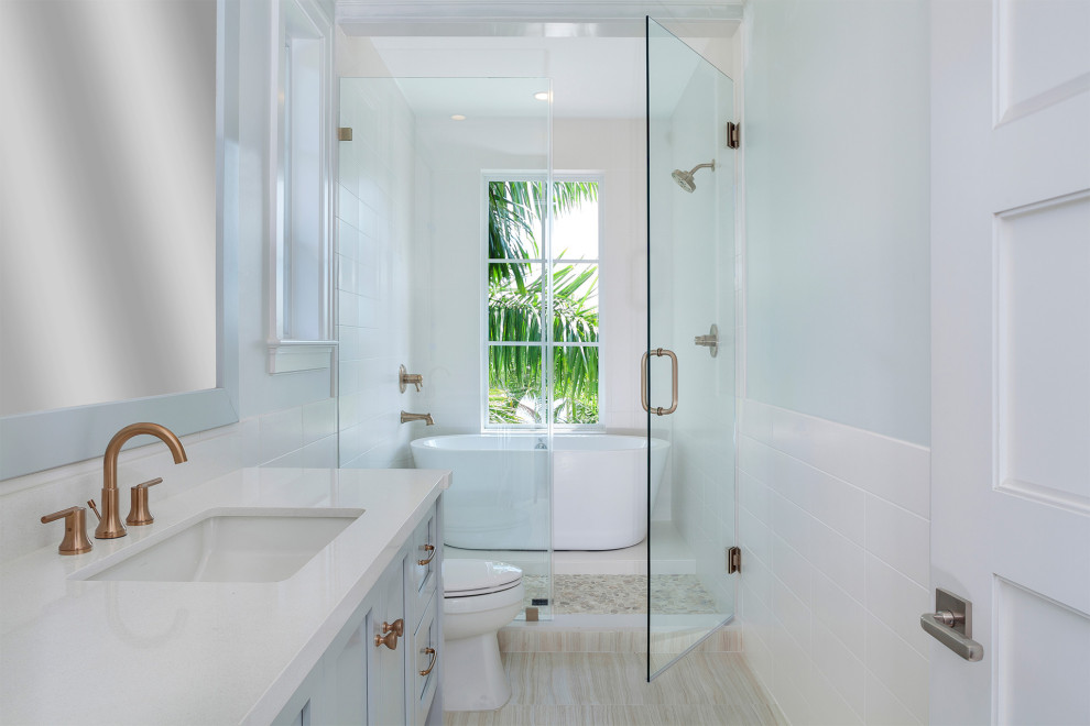 Mid-sized transitional master white tile and porcelain tile porcelain tile and beige floor freestanding bathtub photo in Miami with shaker cabinets, blue cabinets, a one-piece toilet, multicolored walls, an undermount sink, solid surface countertops, a hinged shower door and white countertops