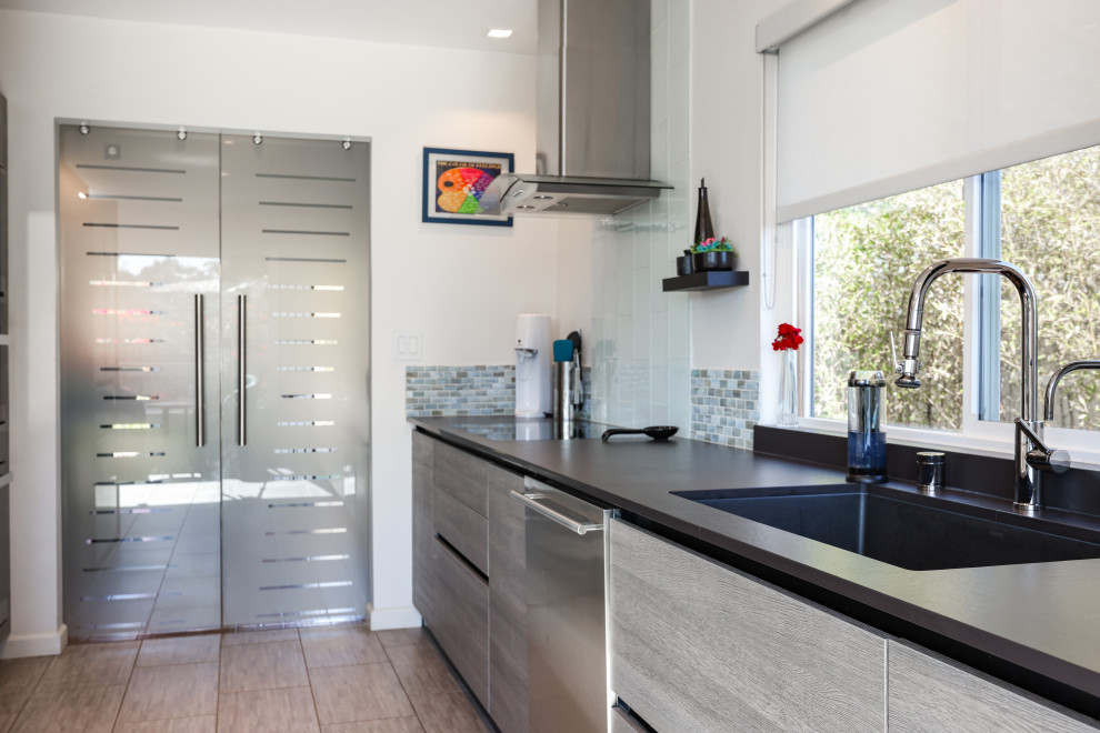 Photo of a midcentury galley eat-in kitchen in San Diego with an undermount sink, flat-panel cabinets, turquoise cabinets, quartz benchtops, multi-coloured splashback, mosaic tile splashback, stainless steel appliances, porcelain floors, grey floor and black benchtop.