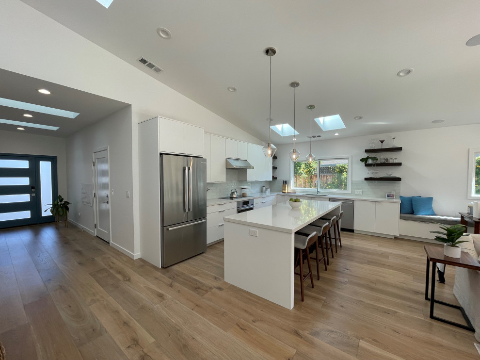 Expansive contemporary l-shaped kitchen/diner in San Francisco with a single-bowl sink, flat-panel cabinets, white cabinets, engineered stone countertops, white splashback, engineered quartz splashback, stainless steel appliances, medium hardwood flooring, an island, brown floors, a vaulted ceiling and grey worktops.