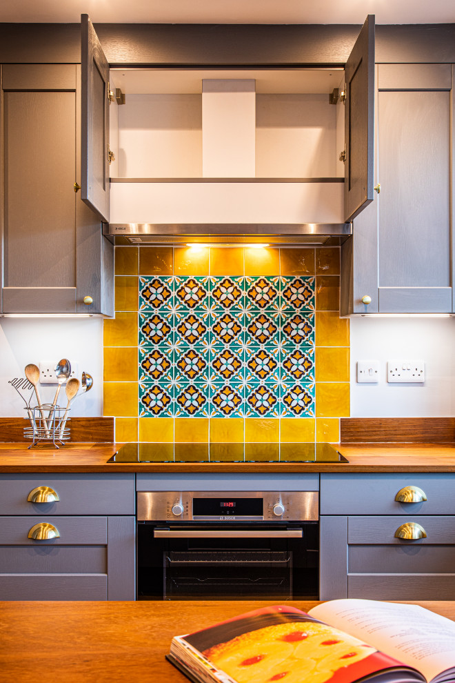 Mid-sized eclectic u-shaped eat-in kitchen in Other with an undermount sink, shaker cabinets, grey cabinets, wood benchtops, yellow splashback, terra-cotta splashback, a peninsula, brown floor and brown benchtop.