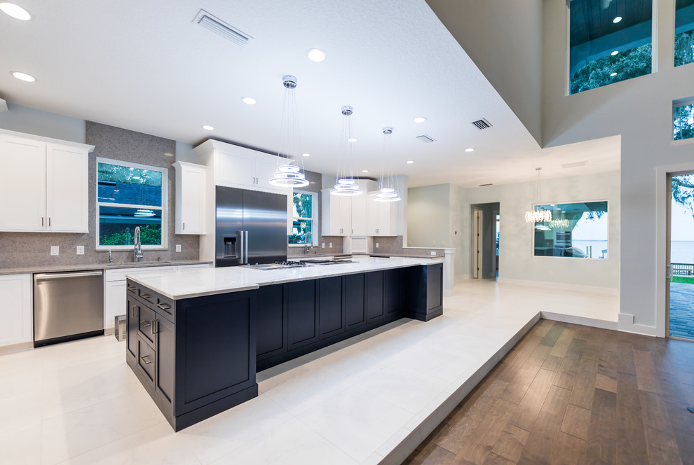 This is an example of a large mediterranean u-shaped kitchen pantry in Jacksonville with flat-panel cabinets, marble benchtops, grey splashback, stone slab splashback, stainless steel appliances, porcelain floors, with island, white floor, white benchtop, an undermount sink and white cabinets.