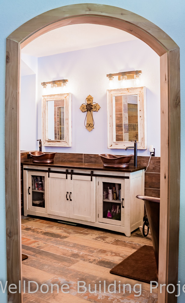 Mid-sized country master bathroom in Houston with furniture-like cabinets, white cabinets, a freestanding tub, a corner shower, a one-piece toilet, brown tile, ceramic tile, blue walls, ceramic floors, a vessel sink, wood benchtops, brown floor and an open shower.