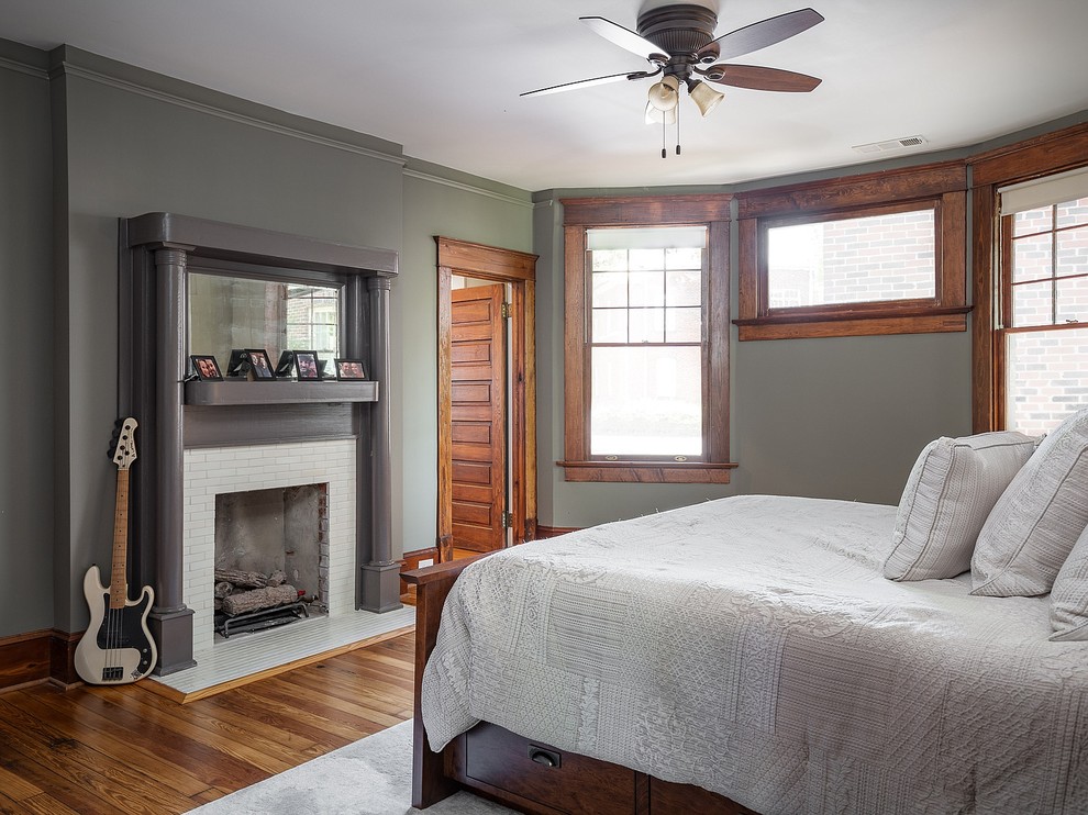 Inspiration for a large arts and crafts master bedroom in Atlanta with grey walls, light hardwood floors, a standard fireplace, a brick fireplace surround and brown floor.