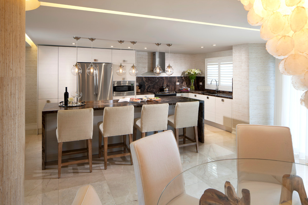 This is an example of a beach style l-shaped eat-in kitchen in Miami with an undermount sink, flat-panel cabinets, white cabinets, brown splashback, stone slab splashback and stainless steel appliances.