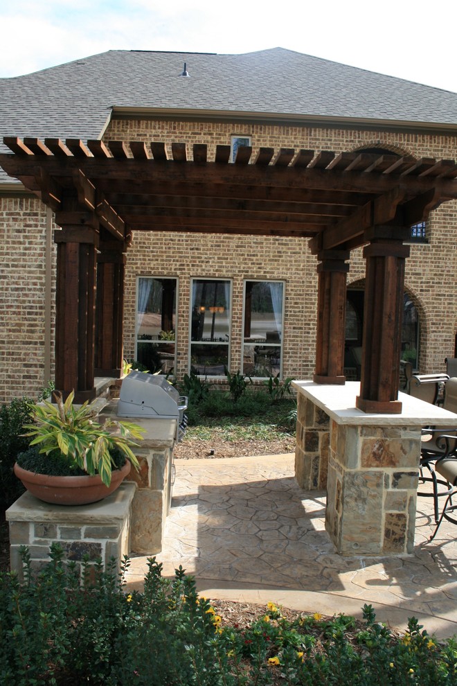 Design ideas for a mid-sized traditional backyard patio in Dallas with an outdoor kitchen, stamped concrete and a pergola.