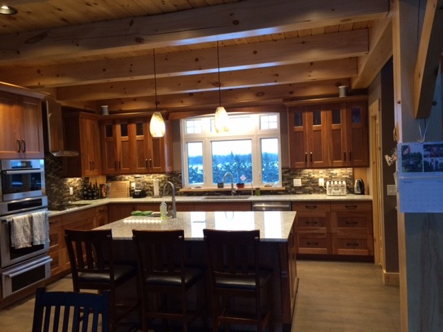 Example of a mountain style light wood floor kitchen design with an undermount sink, raised-panel cabinets, medium tone wood cabinets, quartz countertops, multicolored backsplash, mosaic tile backsplash, stainless steel appliances and an island