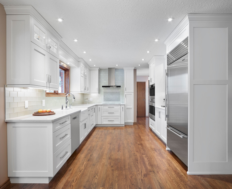 Mid-sized transitional l-shaped medium tone wood floor and brown floor eat-in kitchen photo in Edmonton with a farmhouse sink, recessed-panel cabinets, white cabinets, quartz countertops, gray backsplash, glass tile backsplash, stainless steel appliances and no island