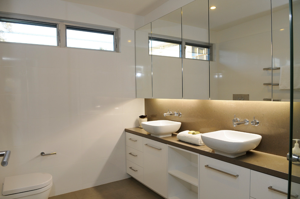 This is an example of a large contemporary kids bathroom in Sydney with flat-panel cabinets, white cabinets, an alcove shower, a one-piece toilet, white tile, porcelain tile, white walls, travertine floors, a vessel sink, engineered quartz benchtops, brown floor, a hinged shower door and brown benchtops.