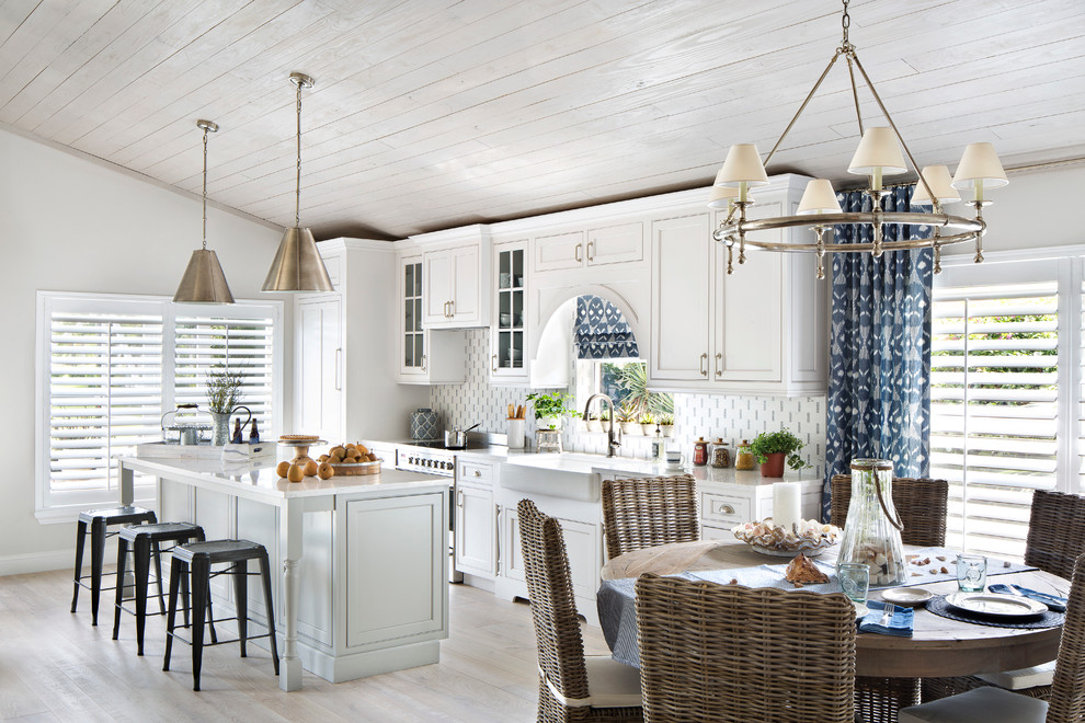 Inspiration for a mid-sized beach style single-wall open plan kitchen in Miami with a farmhouse sink, shaker cabinets, white cabinets, with island, quartz benchtops, multi-coloured splashback, glass tile splashback, stainless steel appliances and porcelain floors.