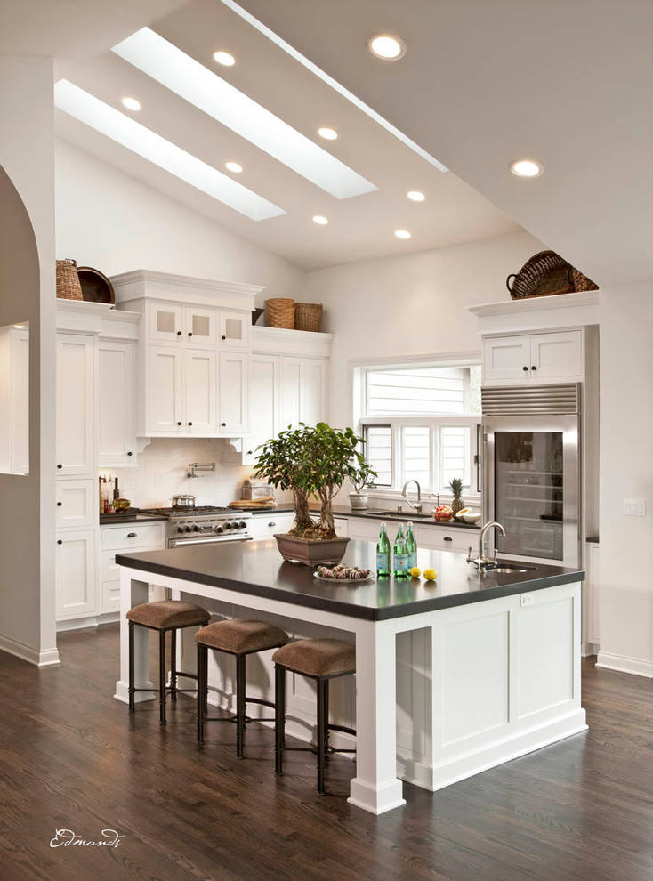 Example of a transitional l-shaped dark wood floor kitchen design in Milwaukee with an undermount sink, recessed-panel cabinets, white cabinets, white backsplash, stainless steel appliances and an island