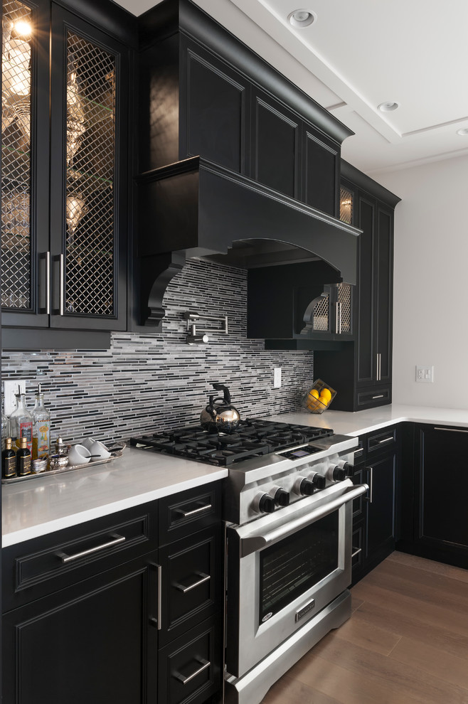 Large transitional u-shaped medium tone wood floor and brown floor kitchen pantry photo with an undermount sink, recessed-panel cabinets, black cabinets, quartz countertops, gray backsplash, glass tile backsplash, stainless steel appliances, an island and white countertops